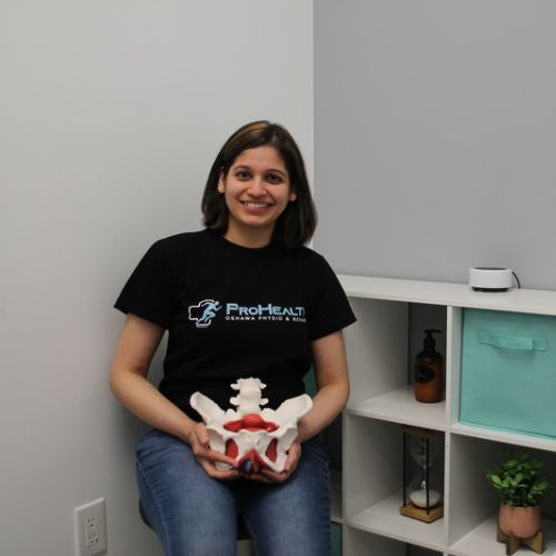 Manu Mrunmayi Sahasrabudhe, Registered Physiotherapist at ProHealth Oshawa Physiotherapy Clinic Oshawa, she is sitting in the clinic chair with the pelvic floor anatomy model to showcase the anatomy of human pelvic floor